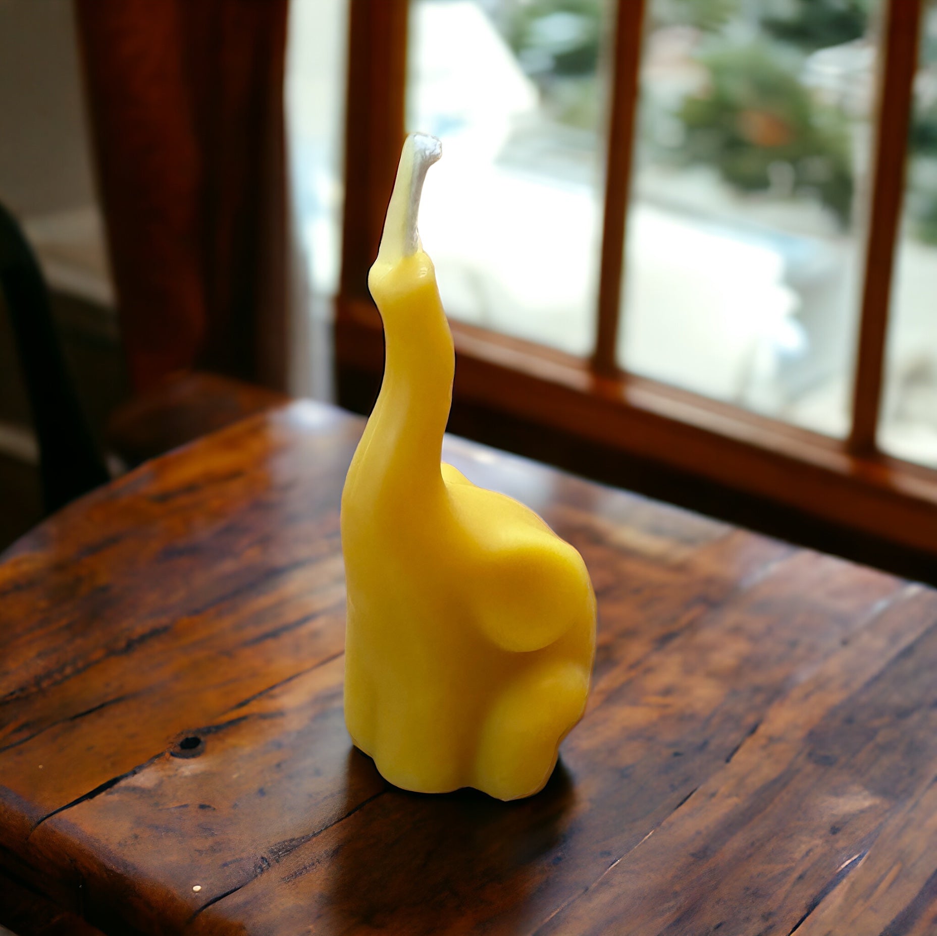 Small beeswax candle in the shape of an elephant on a wooden surface in front of a window